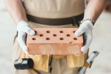 cropped image of builder in protective gloves holding brick  clipart