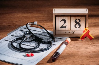 selective focus of wooden calendar with 28th jule date, medical questionnaire, pills, stethoscope, test flask with blood sample, world hepatitis day concept clipart