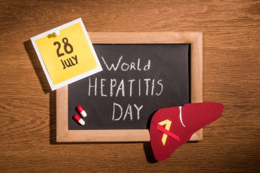 top view of blackboard with lettering world hepatitis day, liver, pills and stick it with lettering 28th july on table clipart