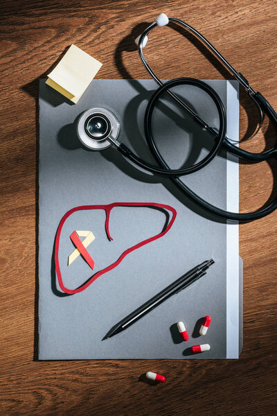 top view of folder, pills, stethoscope, empty stick it and liver with ribbon on table, world hepatitis day concept