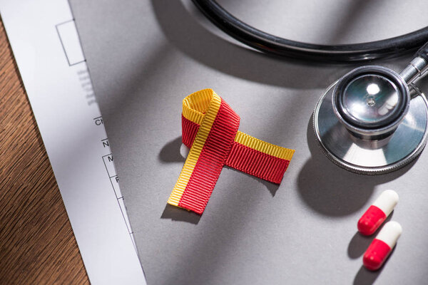 selective focus of ribbon, stethoscope, pills and folder on table, world hepatitis day concept