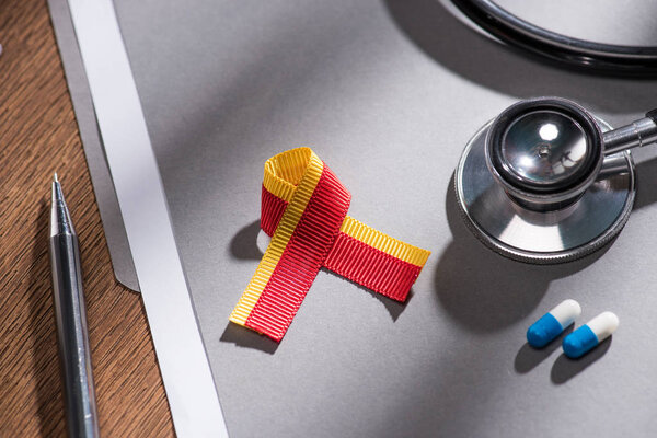 selective focus of ribbon, stethoscope, pills and folder with pen on table, world hepatitis day concept