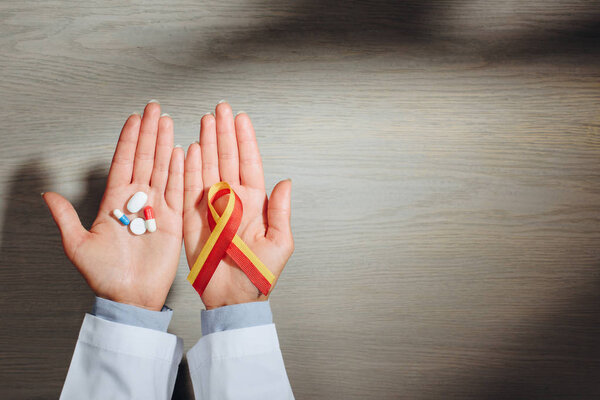 partial view of female doctor holding ribbon and pills, world hepatitis day concept