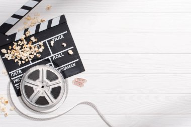 flat lay with clapper board, filmstrips, popcorn and retro cinema tickets arranged on white wooden tabletop clipart