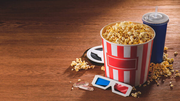 close up view of paper bucket with popcorn, soda drink, 3d glasses on wooden tabletop