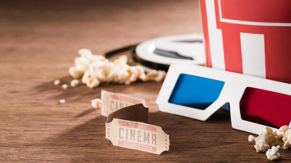 close up view of paper bucket with popcorn, retro cinema tickets and 3d glasses on wooden tabletop
