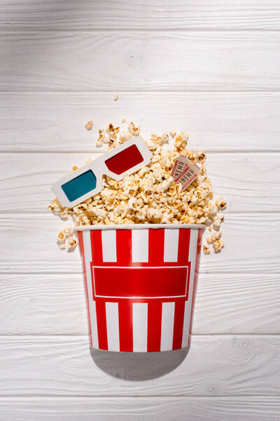flat lay with disposable bucket with popcorn, retro cinema tickets and 3d glasses on white wooden surface