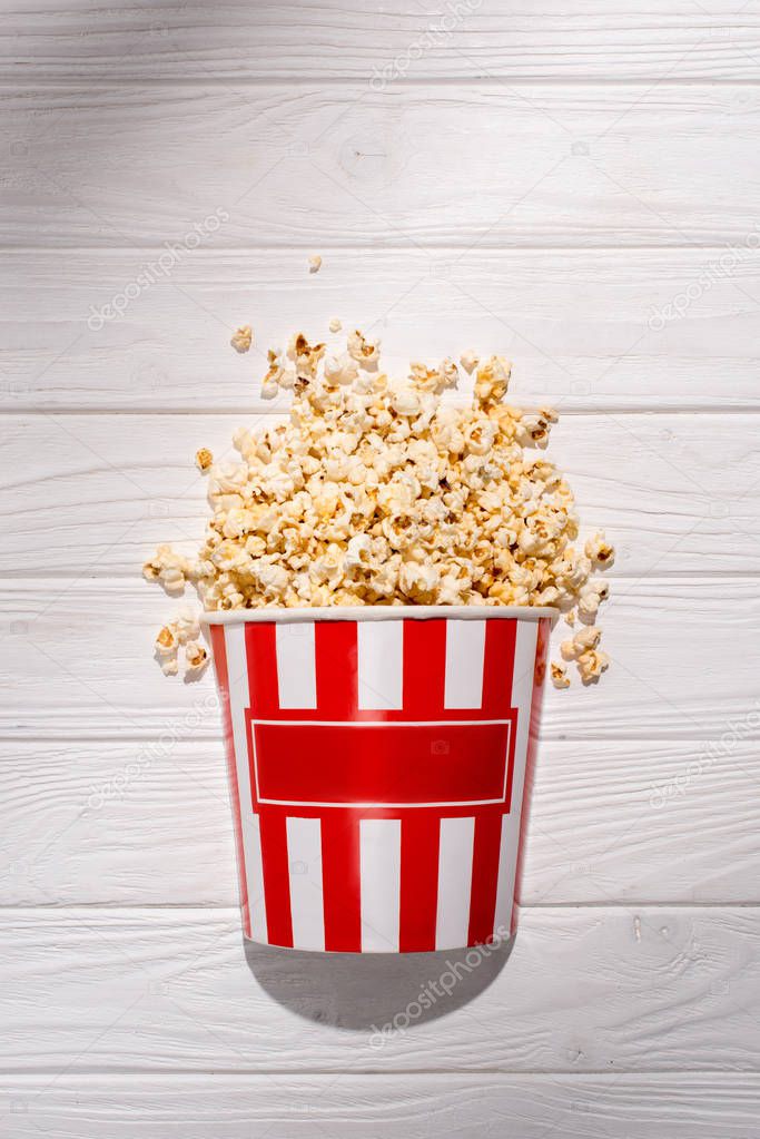 flat lay with disposable bucket with popcorn on white wooden surface