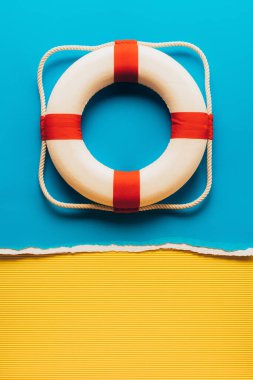 top view of red and white life saver on blue and yellow paper background clipart