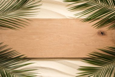 top view of palm leaves and wooden plank on sandy surface clipart
