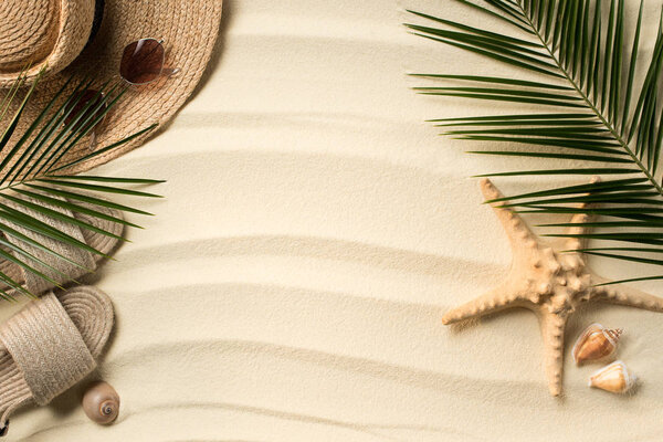 Плоская лежала с пальмовыми листьями, соломенной шляпой и флип-флопами на песчаном пляже
