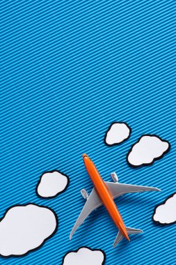 top view of toy plane and paper clouds on blue backdrop, trip concept