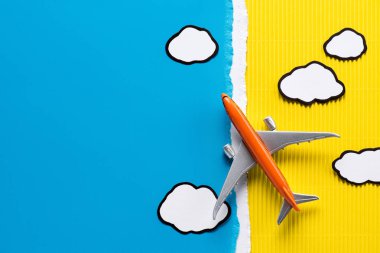 top view of toy plane and paper clouds on yellow and blue background, trip concept clipart