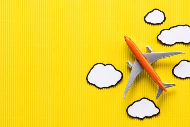 top view of toy plane and paper clouds on yellow background, trip concept