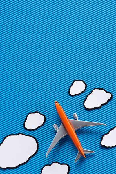top view of toy plane and paper clouds on blue backdrop, trip concept