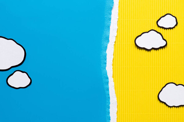top view of paper clouds on blue and yellow paper background