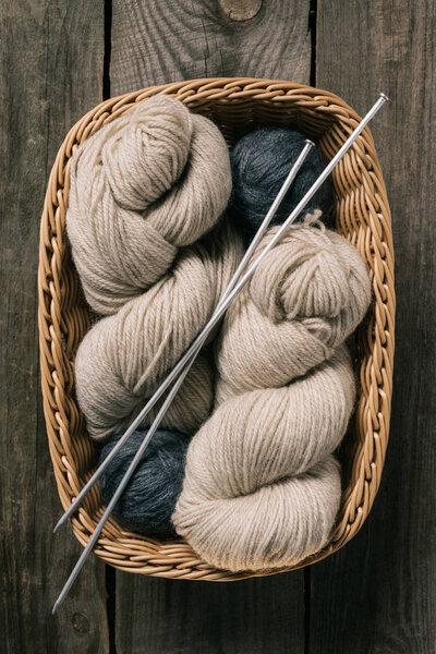 top view of beige and grey knitting yarn wit knitting needles in wicker basket on wooden background 