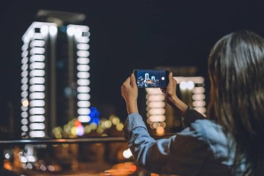 Geceleri smartphone elinde kadın alarak resim şehrin görünümünü geri