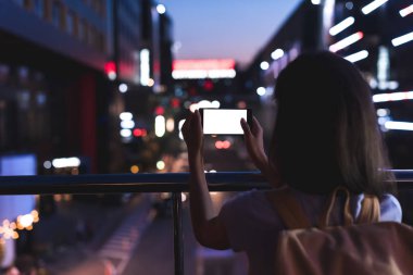 sırt çantası ile kadın ve smartphone ile gece şehir sokak üzerinde duran elinde boş ekran görünümünü geri