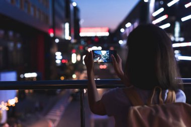 arkadan görünüşü kadın geceleri ellerinde şehir Smartphone cep telefonu ile resim çekmek sırt çantası ile