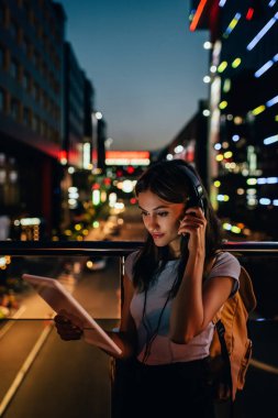 gece şehir ışıkları arka plan üzerinde ile sokakta tablet kullanma kulaklıklar kadında portresi