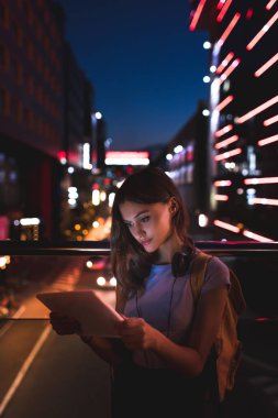 gece şehir ışıkları arka plan üzerinde ile sokakta tablet kullanma kulaklıklar ile genç kadın portresi