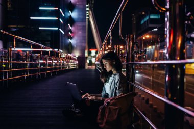 gece şehir ışıkları arka plan üzerinde ile sokakta dizüstü bilgisayar kullanan genç kadın yan görünüm