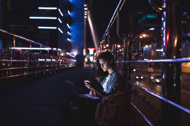 diz arka plan üzerinde gece city ile smartphone kullanarak dizüstü bilgisayar ile genç kadın yan görünüm
