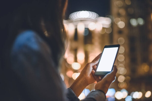 partial view of woman using smartphone with blank screen and night city lights on background