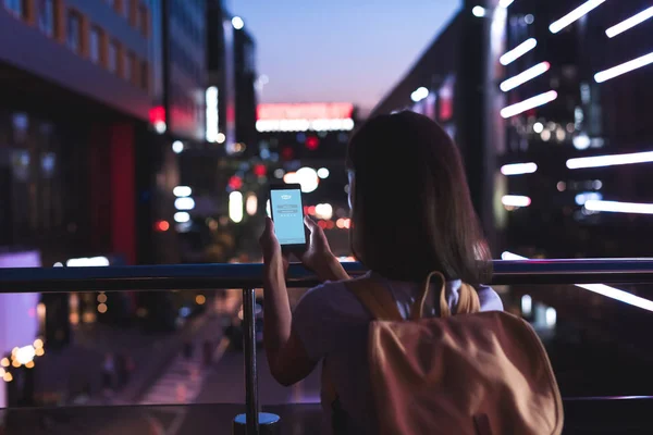 背面的妇女与背包和智能手机与 Skype 标志在屏幕上的手站在夜间城市街 — 图库照片