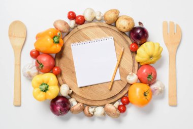 top view of ripe vegetables around wooden board, notebook and pencil isolated on white clipart