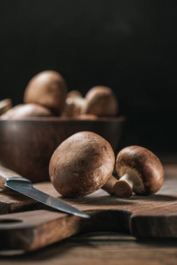 ripe portobello mushrooms and knife on cutting board isolated on black clipart