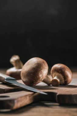 ripe portobello mushrooms and knife on wooden table isolated on black clipart