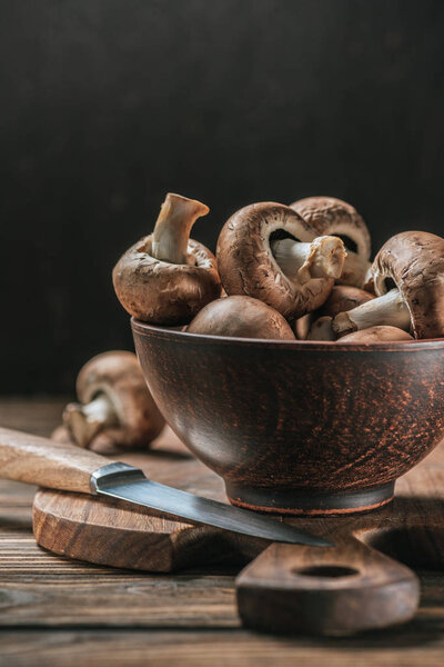 ripe cremini mushrooms in bowl on wooden table isolated on black 