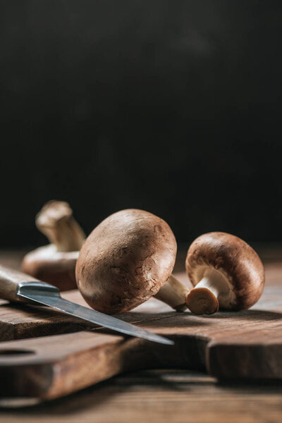ripe portobello mushrooms and knife on wooden table isolated on black