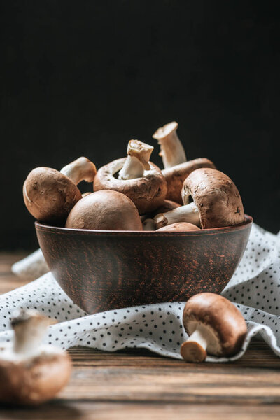 ripe champignon mushrooms in bowl on wooden table isolated on black 
