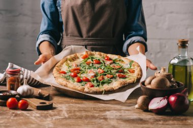 kısmi görünümü önlüğü pişmiş holding Pizza'da ahşap masa ve malzemeler içinde kadın