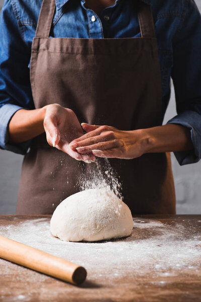 cropped shot of woman in apron kneading dough for pizza