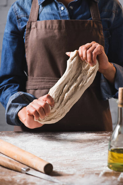 cropped shot of woman in apron kneading dough for pizza