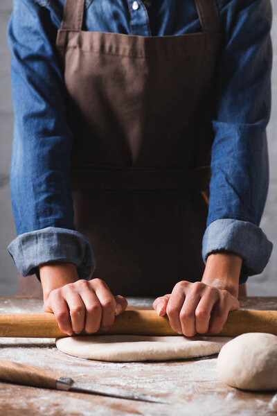 partial view of woman with rolling pin kneading dough for pizza