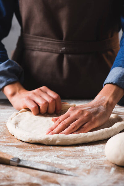 partial view of woman in apron kneading dough for pizza