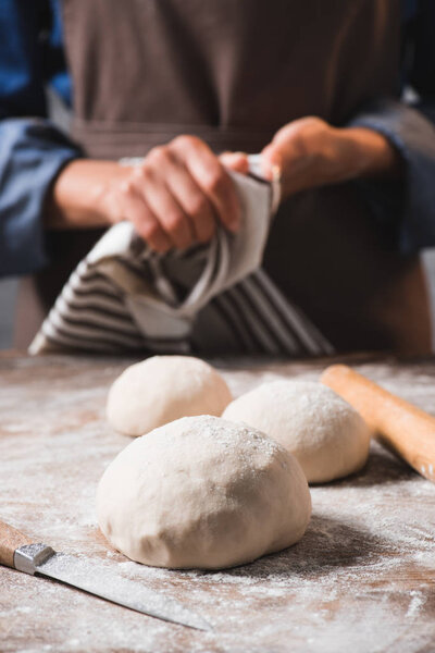selective focus of raw dough for pizza on surface and woman with linen