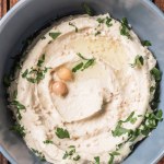 Top view of hummus with parsley and chickpeas in bowl on wooden tabletop