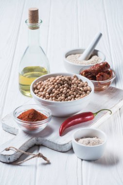 Close up view of raw chickpeas, spices, chili pepper, dried tomatoes and olive oil (hummus ingredients) on wooden tabletop clipart