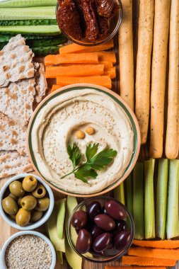 top view of hummus in bowl with arranged cut vegetables slices, breadsticks, olives and pita bread clipart