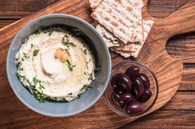 kesme tahtası ahşap yüzeyde zeytin, pide ve humus maydanoz ve kase nohut ile üstten görünüm