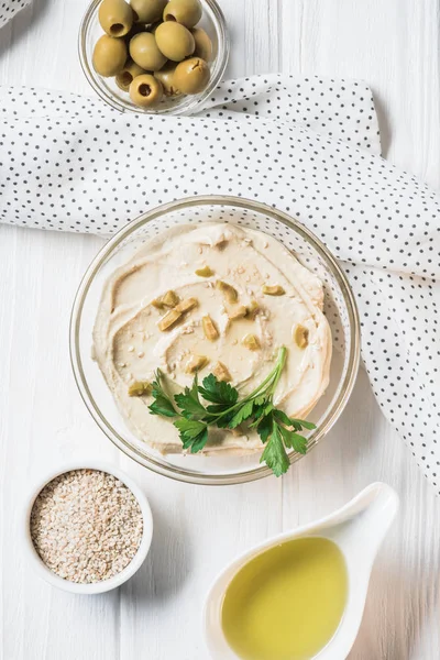 top view of hummus with parsley, olives and spices on wooden tabletop