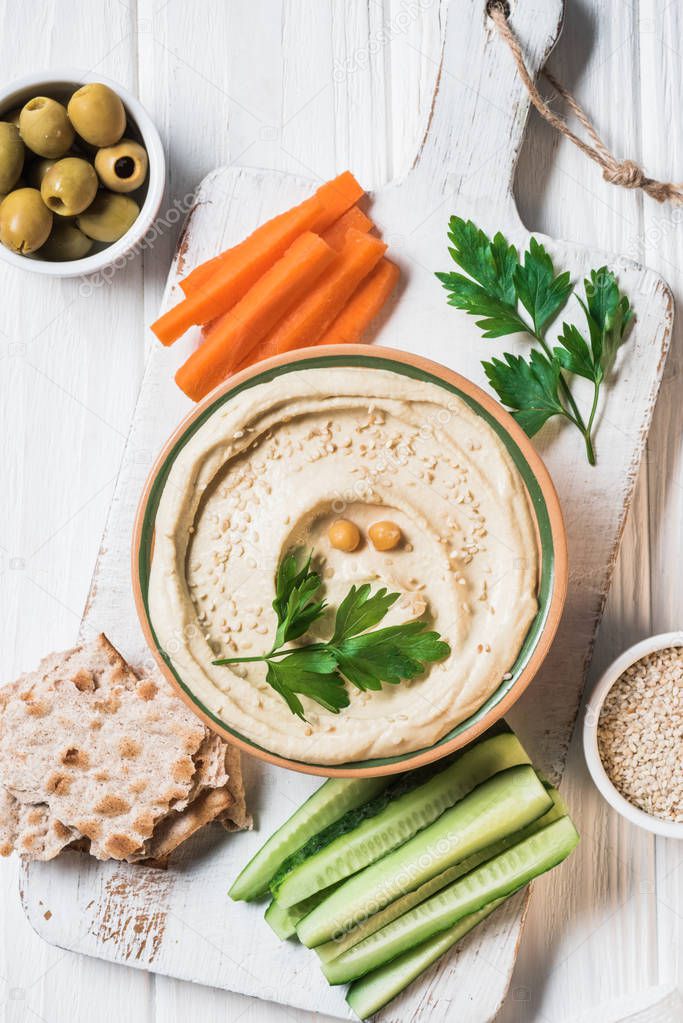 top view of hummus with parsley, cut vegetables and pita bread on wooden tabletop