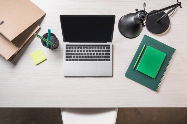 top view of workplace with folders, post it note and laptop with blank screen on table