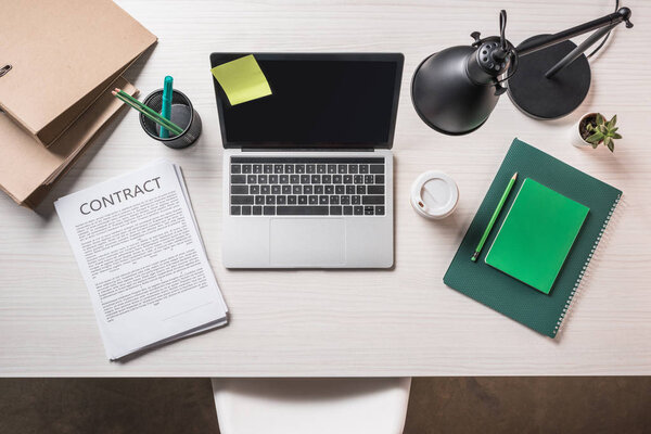 elevated view of laptop, paper cup of coffee, contract and stationery on table 